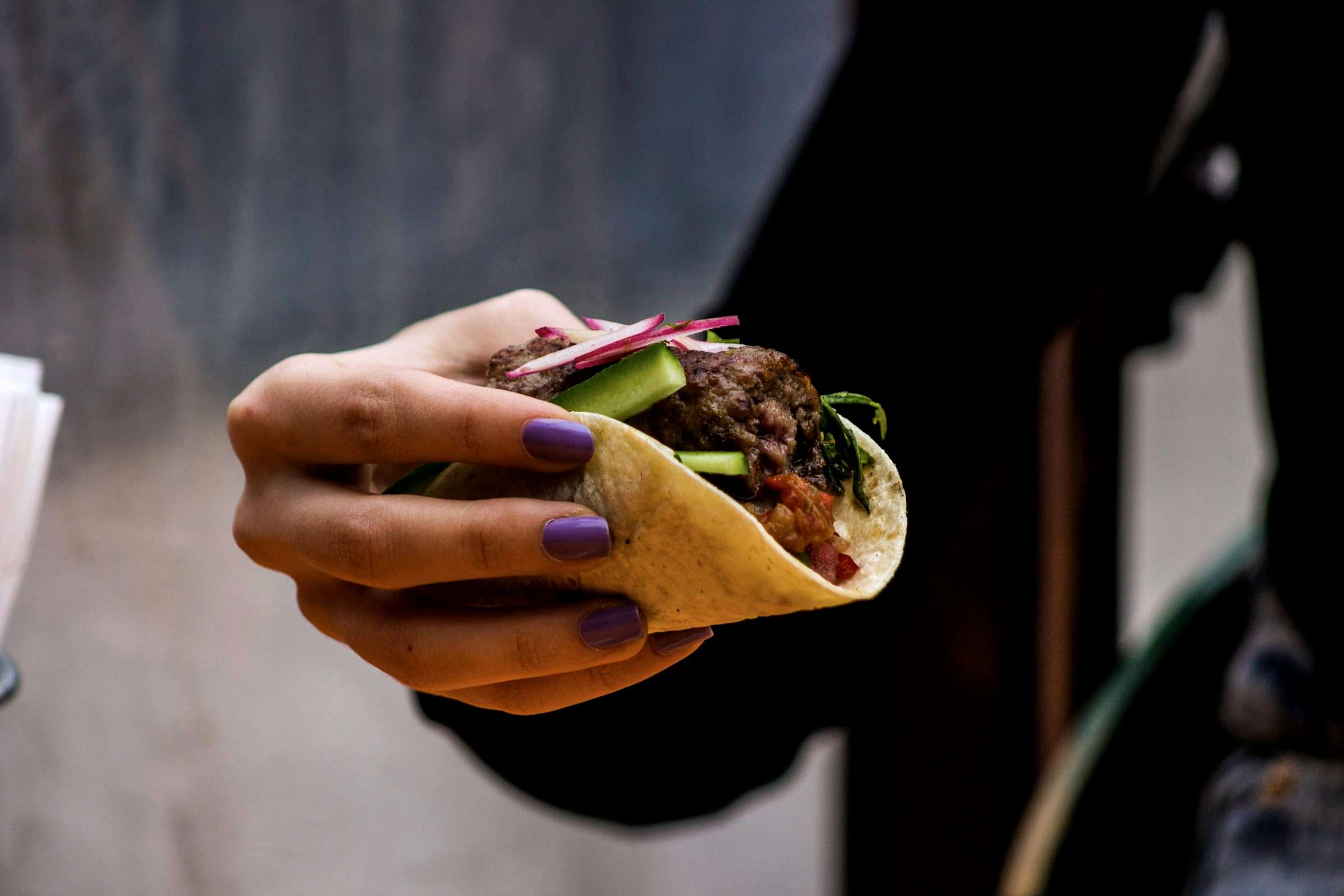Hand hält einen Taco vor dunklem Hintergrund